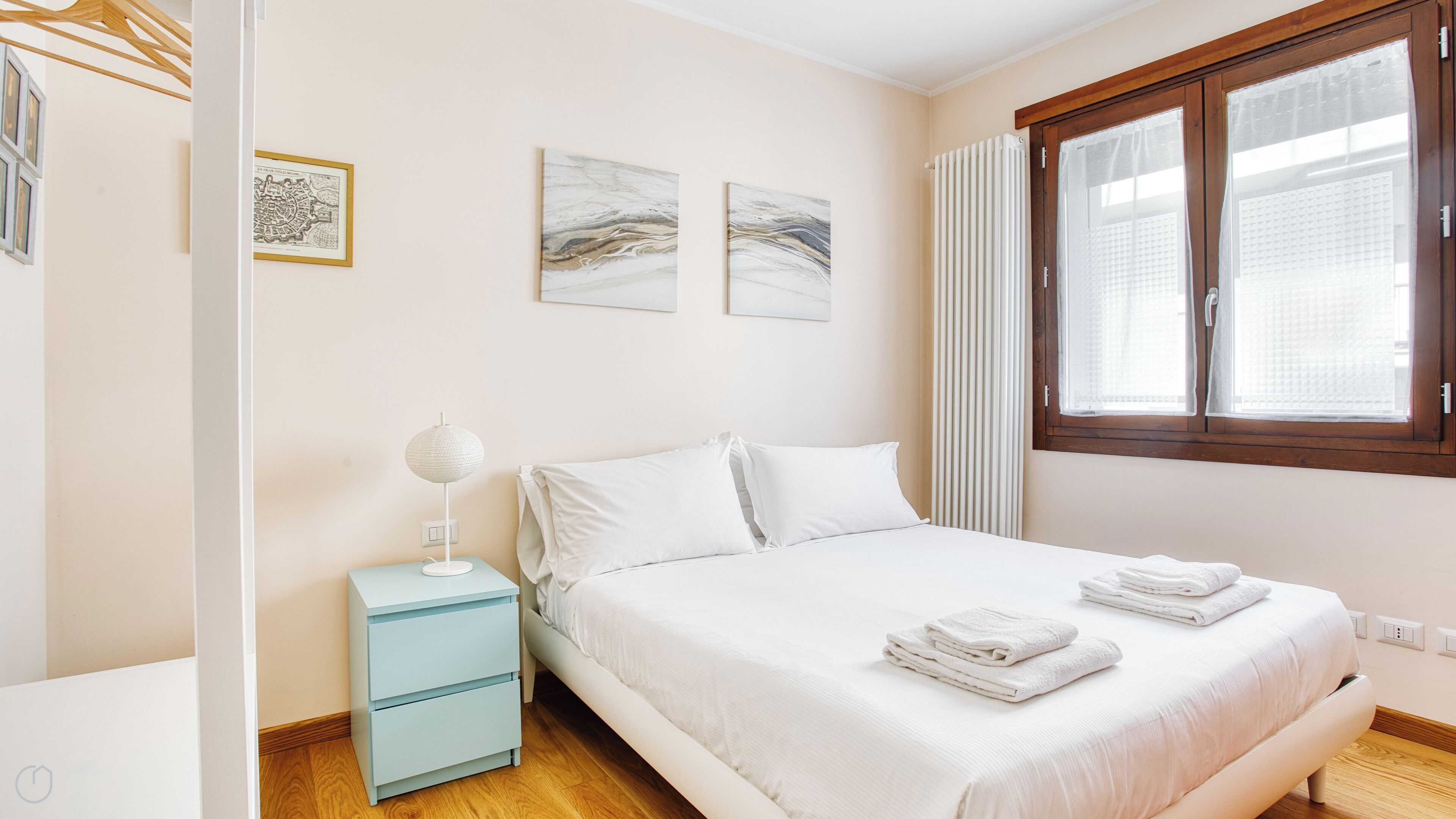 A bedroom with a bed, a nightstand, a lamp, and two wall-mounted artworks.