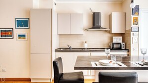 A modern kitchen with white cabinets, a black stove, and a microwave. There are framed pictures on the wall and a dining table with chairs. - Italianway Comfort - Salasco 18 (Milan)