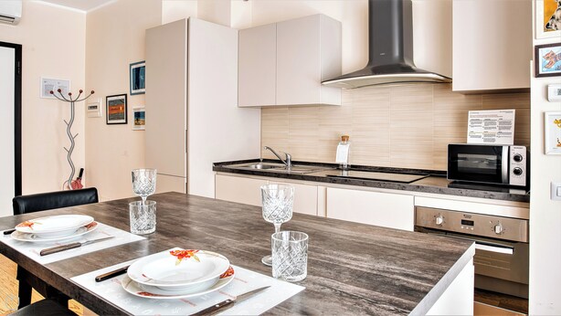 A modern kitchen with a dark countertop, stainless steel appliances, and light-colored cabinetry. - Italianway Comfort - Salasco 18 (Milan)