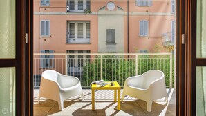 A balcony with two white chairs and a small table, overlooking a building with balconies and windows. - Italianway Comfort - Salasco 18 (Milan)