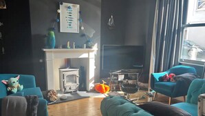 Ein gemütliches Wohnzimmer mit petrolfarbenen Sofas, einem Kamin und einem Fernseher.