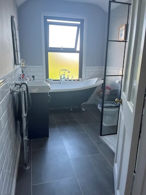 Une salle de bain avec une baignoire, un lavabo et des toilettes. Il y a une fenêtre au-dessus du lavabo et une porte qui donne sur une autre pièce.