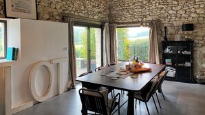 Un coin repas avec un mur en pierre, une table dressée et une vue sur la verdure à l’extérieur.