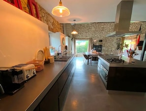 A modern kitchen with a stone wall, a central island, and a dining area with chairs. - Luxury Dordogne Farmhouse - Private SwimmingPool, Parking, Views, Starlink (La Sauvetat-sur-Lède)