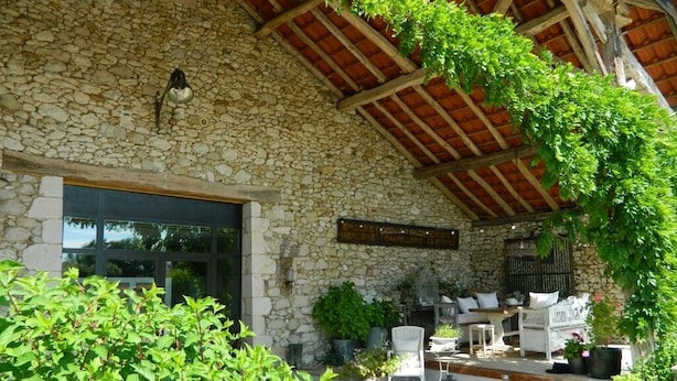 Un bâtiment en pierre doté d’un patio couvert, d’un espace extérieur aménagé pour s’asseoir et de plantes en pot.