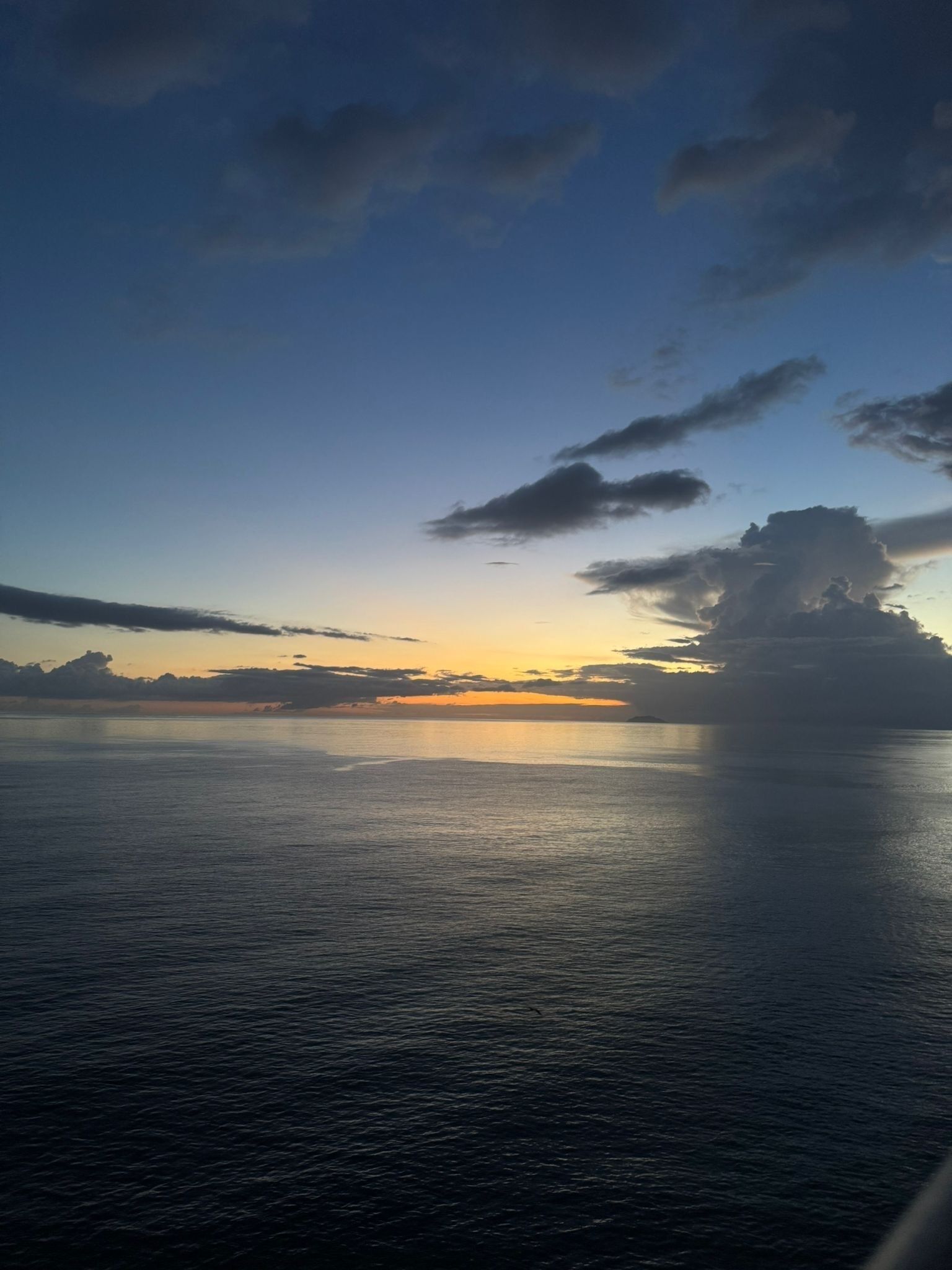 Een rustige zee bij zonsondergang, heldere lucht en enkele wolken.