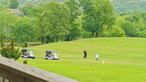 Golfkenttä, jossa on klubitalo, harjoittelualue lyhyitä lyöntejä varten ja taustalla metsäinen kukkula.