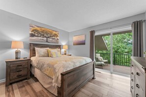 A bedroom with a bed, bedside tables, a dresser, and a balcony with a view of trees. - New Mulligans Escape - Community Pool (Branson)