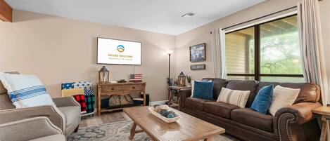 A living room with a brown leather sofa, a wooden coffee table, and a television mounted on the wall.