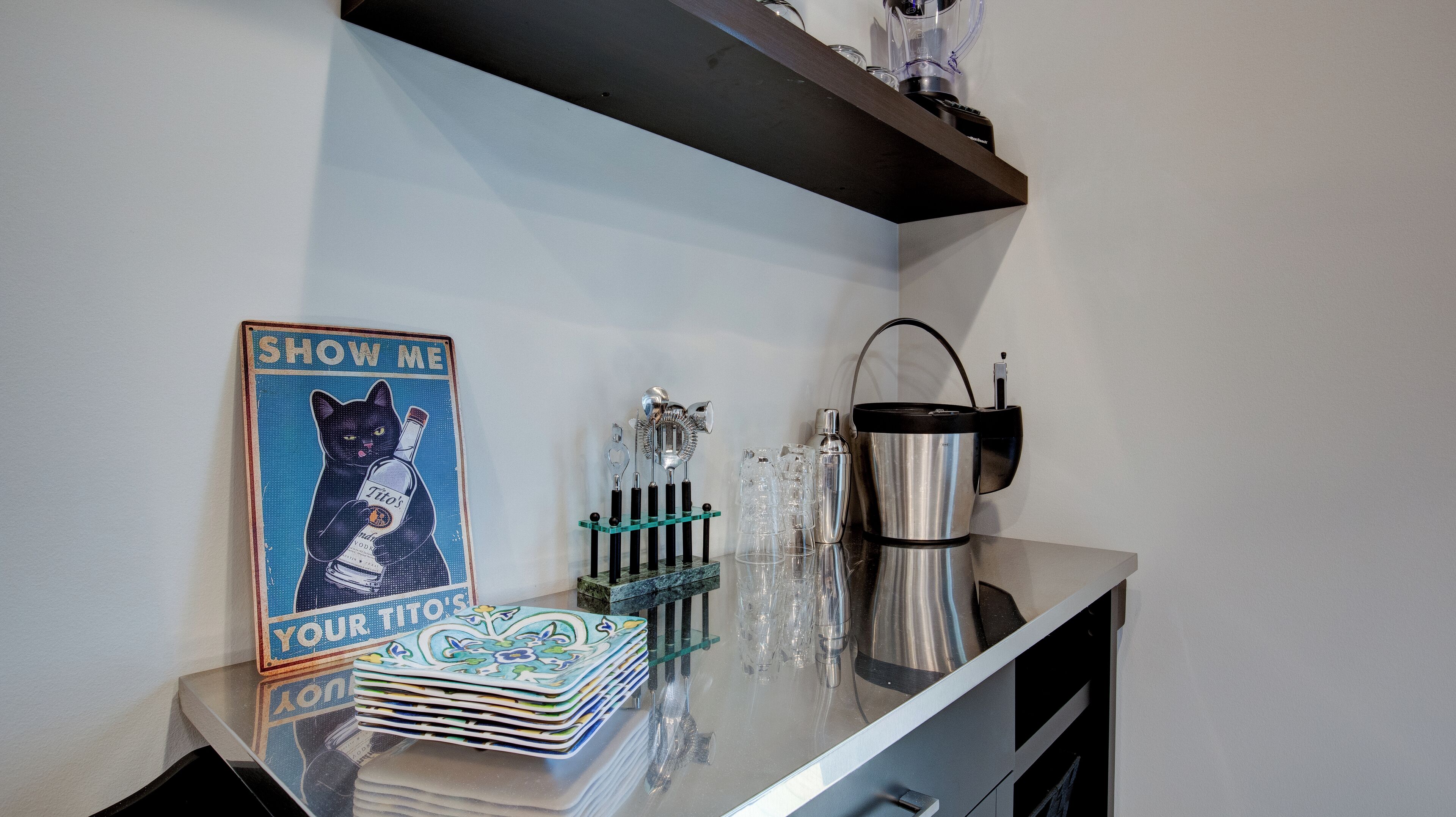 Uma área de bar com um letreiro 'SHOW ME YOUR TITO'S', uma pilha de pratos e uma máquina de café.