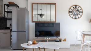 A modern kitchen with a built-in refrigerator, a flat-screen TV, and a dining area with two white tables and clear chairs. - La Lond'ella -  Appt à 1,5km de la mer à Porticcio (Grosseto-Prugna)