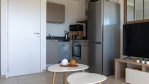 A modern kitchen with stainless steel appliances, a microwave, oven, and a large refrigerator. There is a small round table with a bowl and a fruit. - La Lond'ella -  Appt à 1,5km de la mer à Porticcio (Grosseto-Prugna)