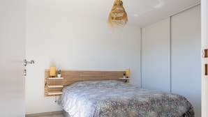 A bedroom with a bed, bedside tables, a hanging light fixture, and a wardrobe. - La Lond'ella -  Appt à 1,5km de la mer à Porticcio (Grosseto-Prugna)