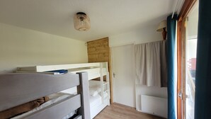 A room with bunk beds, a wooden ceiling, a door, and a window with curtains.