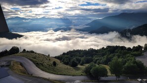 A mountainous landscape with a road curving through a valley, surrounded by clouds and trees.