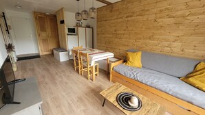 A cozy living area with a wooden sofa, a dining table with chairs, and a small kitchenette.