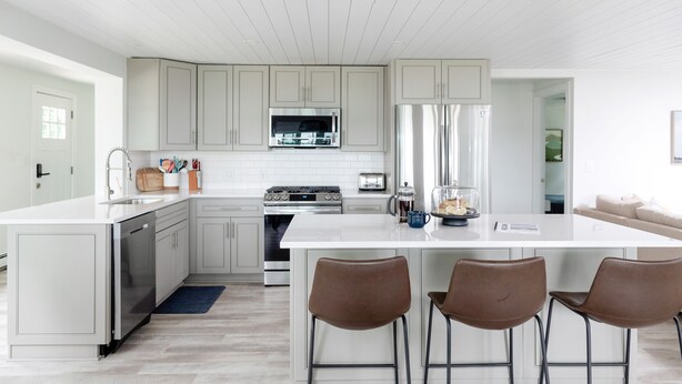 A modern kitchen with white cabinetry, stainless steel appliances, and a central island with bar stools. - Modern Lakefront Gun Lake Cottage Near Bay Pointe Inn (Shelbyville)
