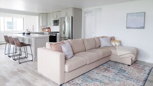 A modern kitchen with a large island, a beige sofa, and a patterned rug. - Modern Lakefront Gun Lake Cottage Near Bay Pointe Inn (Shelbyville)