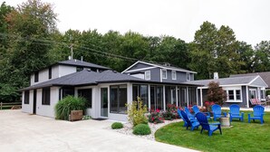 A two-story house with a covered patio area, a front lawn, and blue outdoor chairs. - Modern Lakefront Gun Lake Cottage Near Bay Pointe Inn (Shelbyville)
