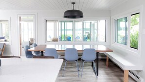 A modern dining area with a large table, four chairs, and a black pendant light. - Modern Lakefront Gun Lake Cottage Near Bay Pointe Inn (Shelbyville)