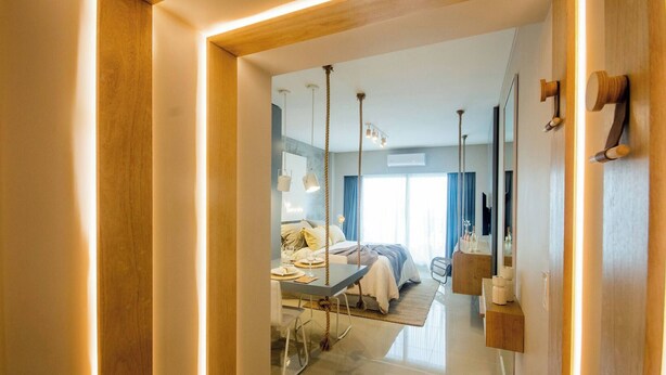 Quarto de hotel moderno com cama, mesa de cabeceira e vista para o corredor.
