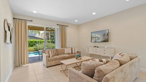A living room with a sofa, a coffee table, and a TV. There is a sliding glass door leading to an outdoor area with a pool. - AMAZING 8 BEDROOMS WITH POOL AND GAME ROOM PERFECT LOCATION! (2308) (Kissimmee)