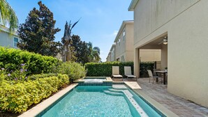A swimming pool with a tiled edge, surrounded by greenery and a patio area with outdoor furniture. - AMAZING 8 BEDROOMS WITH POOL AND GAME ROOM PERFECT LOCATION! (2308) (Kissimmee)