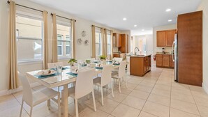 A modern kitchen with wooden cabinets, a central island, and a dining area with a glass table and chairs. - AMAZING 8 BEDROOMS WITH POOL AND GAME ROOM PERFECT LOCATION! (2308) (Kissimmee)