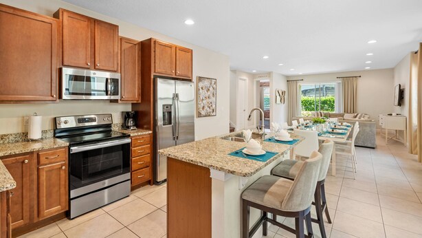 A modern kitchen with granite countertops, stainless steel appliances, wooden cabinets, and a central island with bar stools. - AMAZING 8 BEDROOMS WITH POOL AND GAME ROOM PERFECT LOCATION! (2308) (Kissimmee)