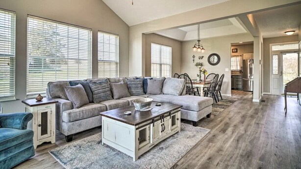 A spacious living room with a sectional sofa, a coffee table, and a dining area with a chandelier. - Charming Family Country Lane Cottage| 3 min to lake (Dandridge)