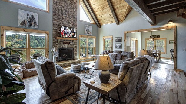 A spacious living room with a stone fireplace, large windows, and a high wooden ceiling. - Luxury Smoky Mountain Cabin | Amazing Views, Hot Tub, Fire Pit Near Pigeon Forge (Sevierville)