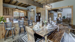 A rustic kitchen with wooden beams, a dining area with a wooden table set for four, and a living room with a sofa and a coffee table. - Luxury Smoky Mountain Cabin | Amazing Views, Hot Tub, Fire Pit Near Pigeon Forge (Sevierville)