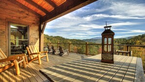 A wooden deck with chairs and a table, overlooking a mountainous landscape. - Luxury Smoky Mountain Cabin | Amazing Views, Hot Tub, Fire Pit Near Pigeon Forge (Sevierville)