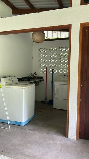 Un cuarto de lavandería con lavadora, secadora y un trapeador apoyado en la pared.
