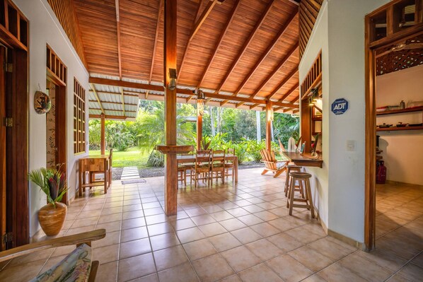 Un espacio al aire libre techado con techo de madera, suelo de baldosas y vista a un jardín exuberante.