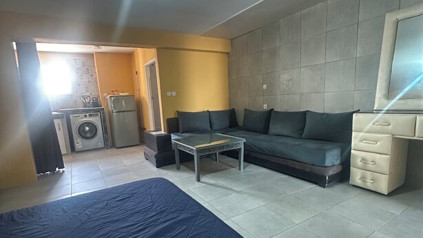 A room with a bed, a sofa, a small table, a washing machine, and a television. - Studio loft waterfront (Haouzia)
