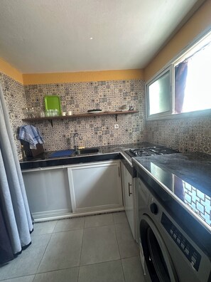 A compact kitchen with a washing machine, a sink, and a window. - Studio Loft by the Water (Haouzia)