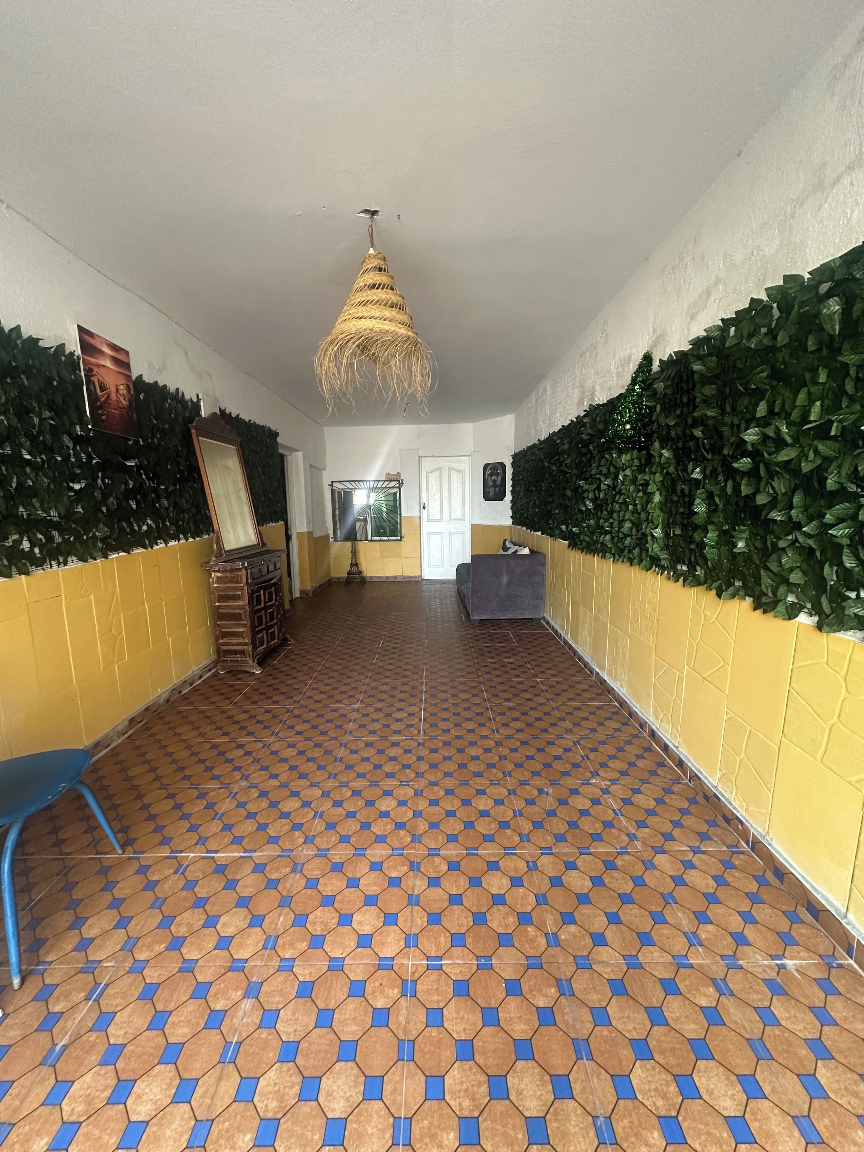 Un pasillo con suelo estampado, una lámpara colgante y paredes cubiertas de hojas verdes.