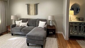 Una sala de estar moderna con un sofá seccional gris, dos mesas auxiliares con lámparas, un adorno de pared y un mueble de madera con espejo.
