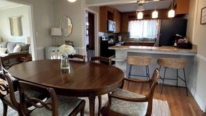 Un comedor con una mesa redonda de madera y cuatro sillas, un pequeño jarrón con flores, y una cocina al fondo.