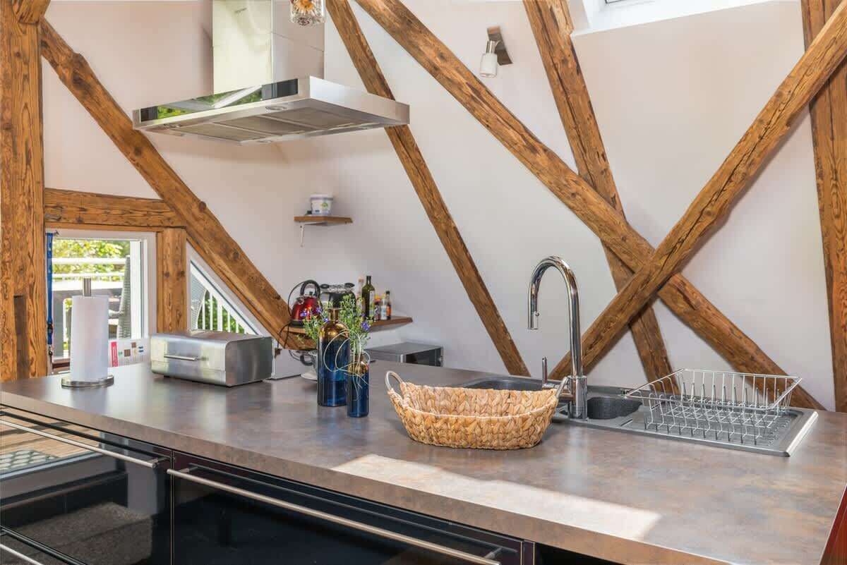 Una cocina moderna con vigas de madera a la vista, un lavaplatos de acero inoxidable y un horno empotrado.