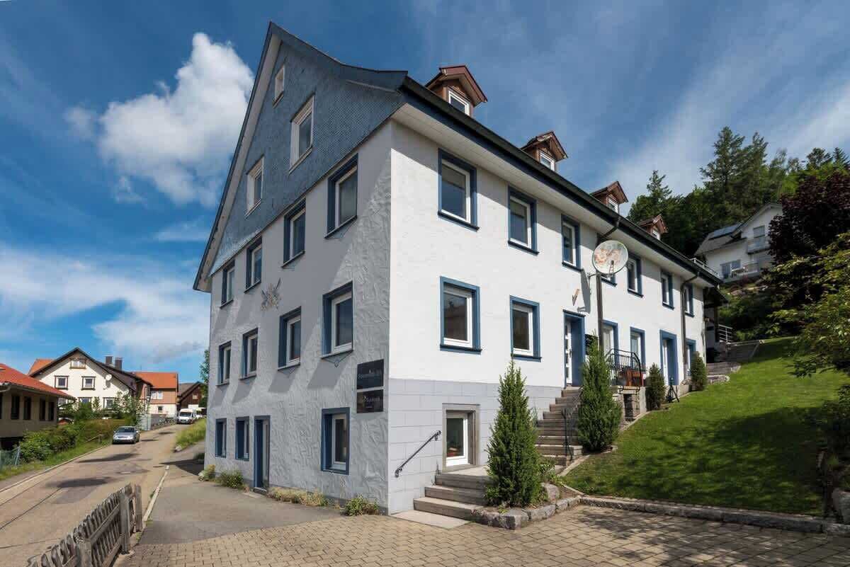 Un edificio de varios pisos con fachada blanca y detalles azules, que presenta una escalera central y un pequeño jardín.