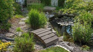 Ein Garten mit Teich, einer Holzbrücke und einer Bank.