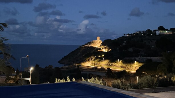 A coastal view with a hilltop structure illuminated by lights, a swimming pool, and a road leading up the hill. - Tiffany Home near Cefalù  (san nicola l'arena)