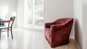 A room with a large sliding glass door leading to an outdoor area, a wooden dining table with chairs, and a red velvet armchair.
