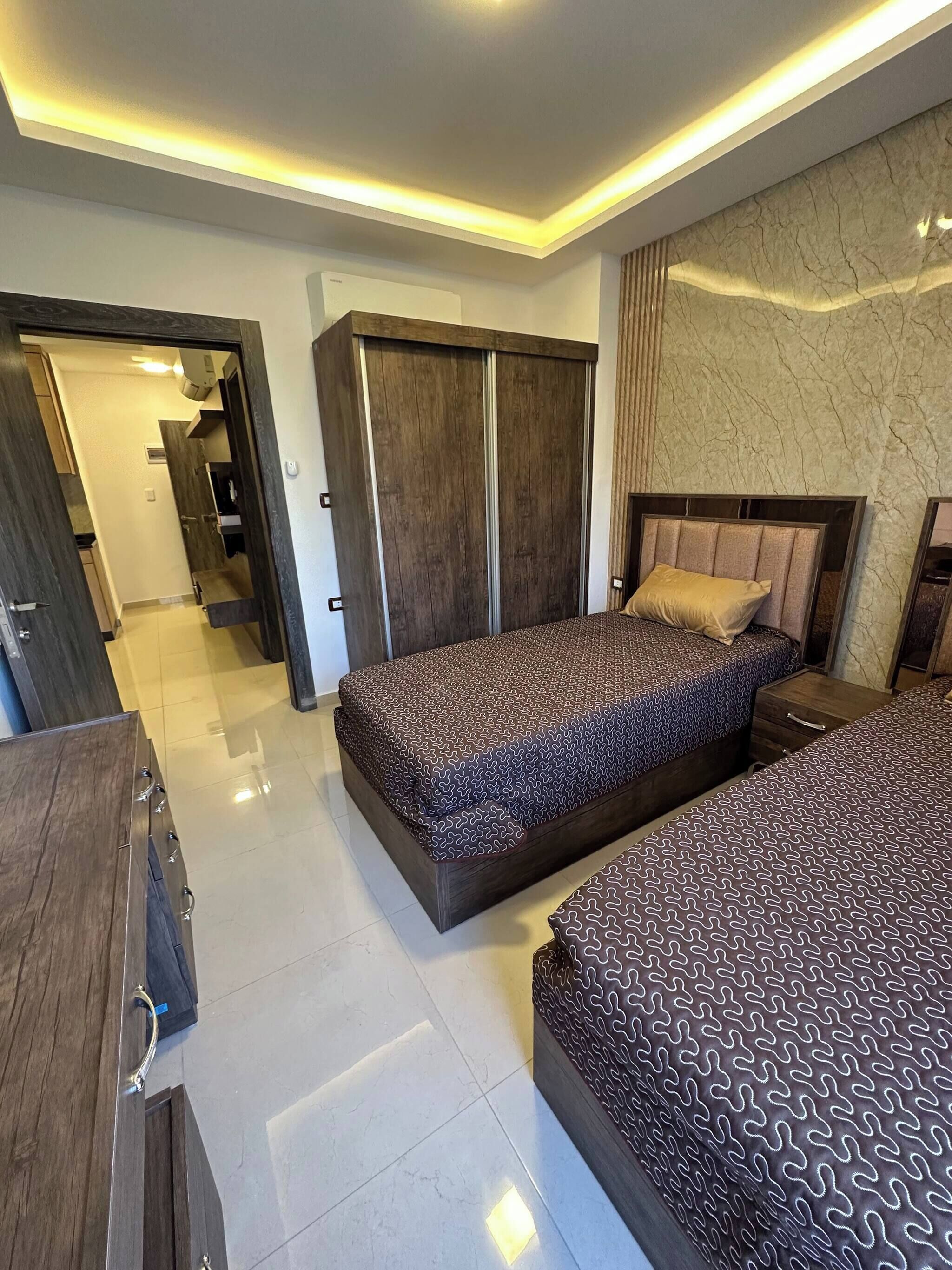 Ein modernes Schlafzimmer mit zwei Betten, einem Kleiderschrank und einem durch eine offene Tür einsehbarer Badezimmer.