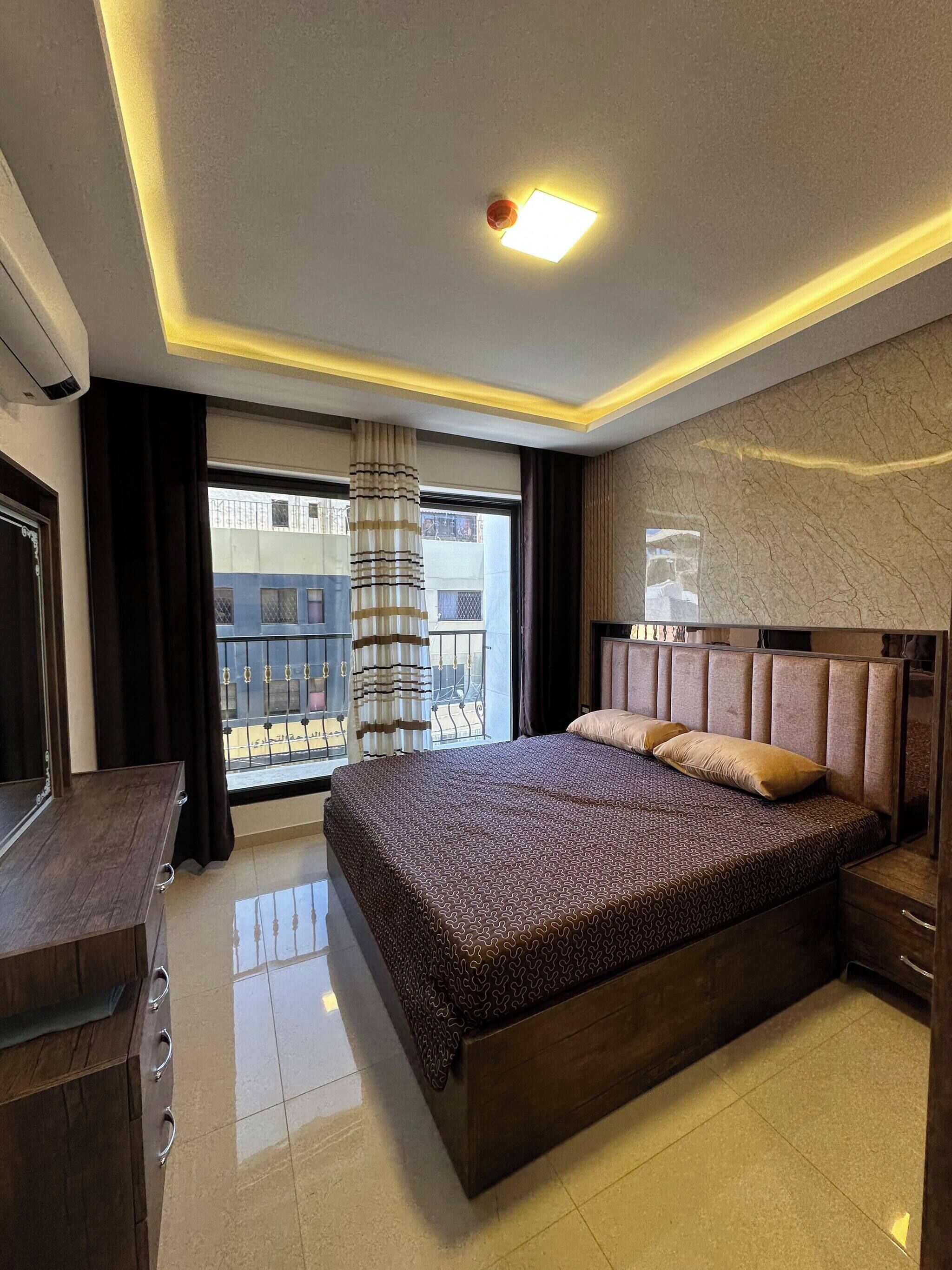 A hotel room with a large bed, a wooden dresser, a mirror, and a view of the outside balcony.