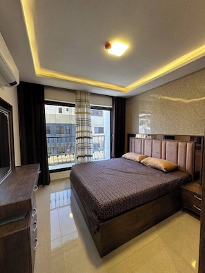 A hotel room with a large bed, a wooden dresser, a mirror, and a view of the outside balcony. - JRE Modern 2bedroom For Rent Abdoun (Amman)