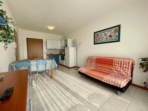 A compact living space with a kitchenette, a dining area with a table and chairs, and a sofa. - Lovely Flat Overlooking the Pool (Caorle)
