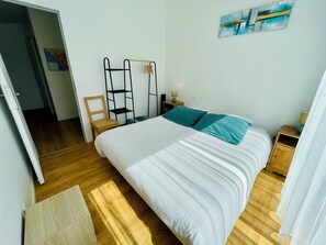 A bedroom with a bed, wooden floor, a chair, a nightstand, and a wall art piece.